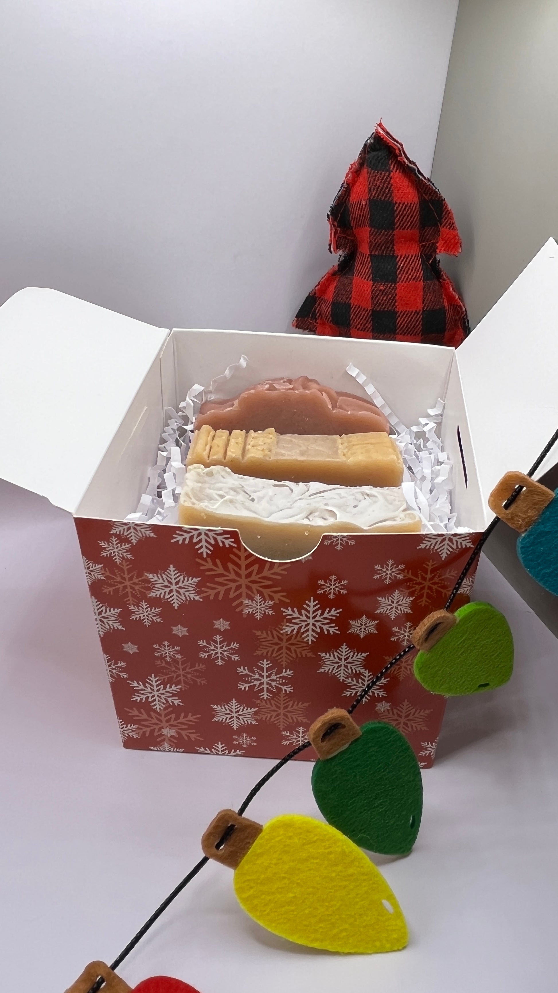 A festive holiday gift set box containing three different scented soaps and a mesh soap saver bag, decorated with Christmas-themed decorations outside the box.